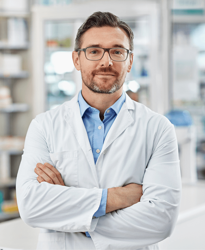 Portrait of a pharmacist standing with his arms crossed in a drugstore. All products have been altered to be void of copyright infringements
