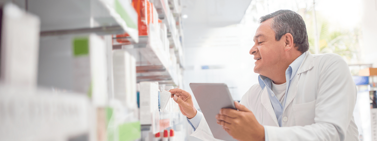 Happy pharmacist doing the inventory at a drugstore using a tablet computer