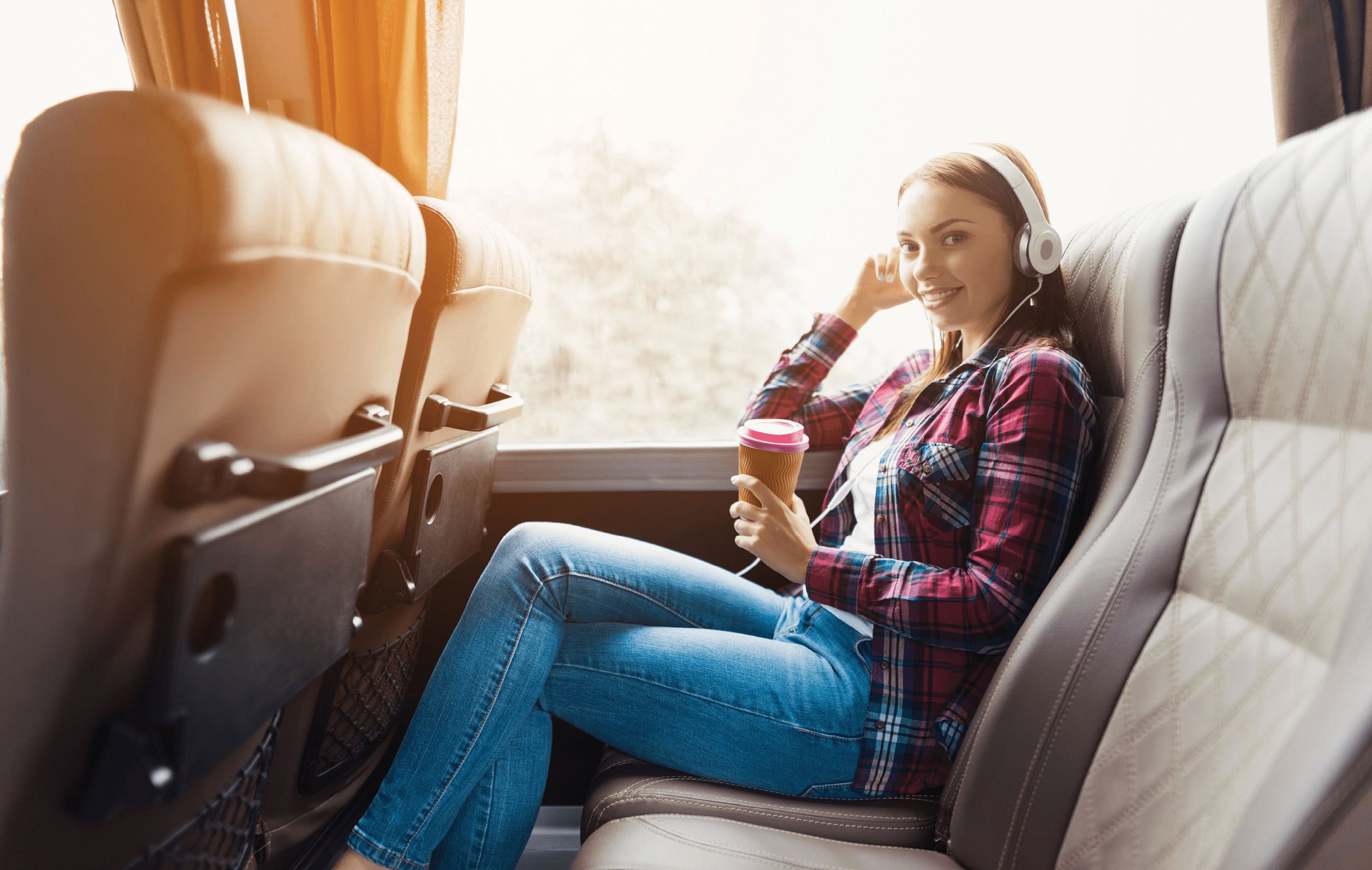 The woman on the passenger seat of the bus listens to music and drinks coffee. She looks out the window and smiles. Outside the window is a beautiful green landscape. 878483660 traveler, country, background, holiday, trip, urban, vacation, white, downtown, view, young, woman, happy, man, concept, lifestyle, person, casual, baggage, sightseeing, outdoor, object, landmark, transport