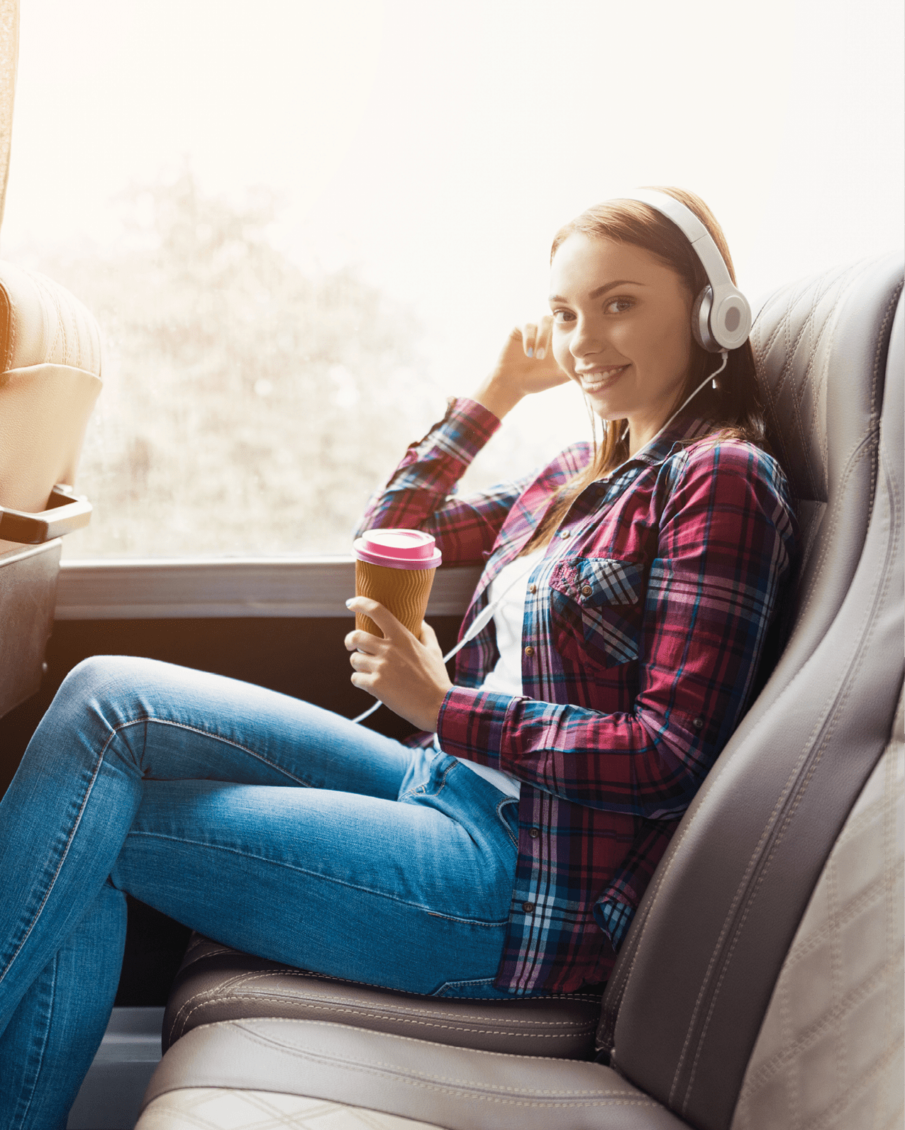 The woman on the passenger seat of the bus listens to music and drinks coffee. She looks out the window and smiles. Outside the window is a beautiful green landscape. 878483660 traveler, country, background, holiday, trip, urban, vacation, white, downtown, view, young, woman, happy, man, concept, lifestyle, person, casual, baggage, sightseeing, outdoor, object, landmark, transport